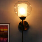 Contemporary Brass Wall Light with clear glass shade mounted on a white wall, featuring a sleek gold finish and modern minimalist design.