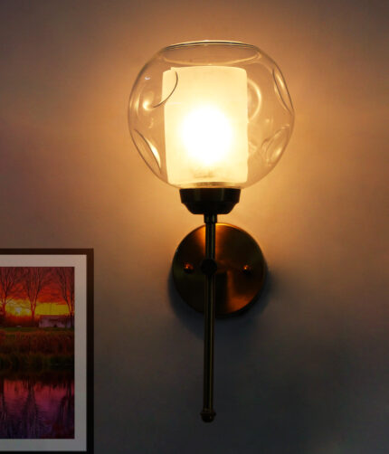 Contemporary Brass Wall Light with clear glass shade mounted on a white wall, featuring a sleek gold finish and modern minimalist design.