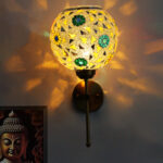 Elegant gold wall-mounted mosaic lamp with spherical glass shade featuring intricate geometric and floral patterns, casting warm ambient light on a modern interior wall.