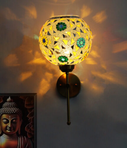 Elegant gold wall-mounted mosaic lamp with spherical glass shade featuring intricate geometric and floral patterns, casting warm ambient light on a modern interior wall.
