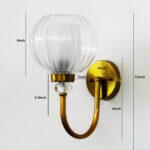 Clear Glass Globe wall sconce with ribbed glass shade and gold curved arm mounted on a white wall