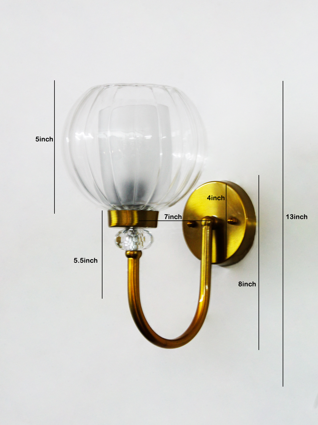 Decorative Brass Wall Light with Clear Glass Globe Clear Glass Globe wall sconce with ribbed glass shade and gold curved arm mounted on a white wall