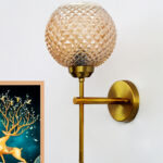 Brass wall light with textured amber glass shade and modern metal arm mounted on wall creating warm ambient lighting