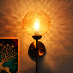 Brass wall light with textured amber glass shade and modern metal arm mounted on wall creating warm ambient lighting