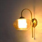 Down Kachori Glass wall light with downward amber glass shade and curved brass arm, glowing warmly on wall
