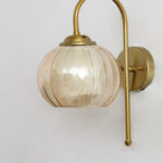 Amber Kharbhuja Glass wall light with ribbed amber glass shade and curved brass arm mounted on wall