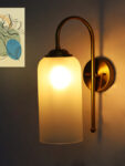 White Milky Froasted Glass wall light with cylindrical frosted glass shade and curved brass arm mounted on wall
