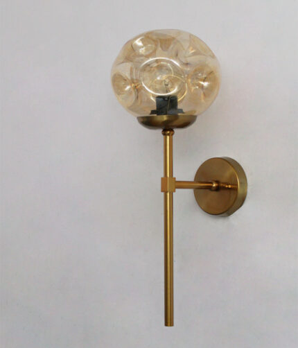 Amber Glass Globe Modern Light wall fixture with textured amber glass globe and brass arm mounted on white wall