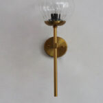 Clear Kharbuja Glass wall light with ribbed transparent glass globe and brass mount on white wall