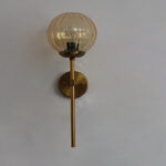 Amber Kharbuja Glass wall light with ribbed amber glass globe and brass mount, glowing warmly on wall