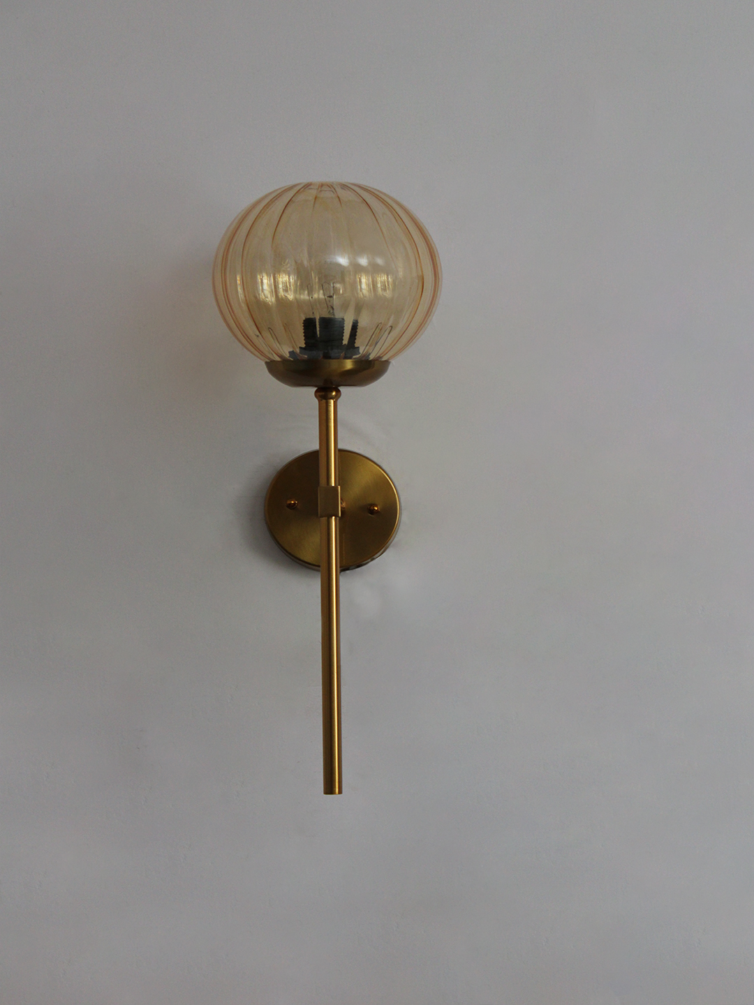 Contemporary Brass Funner Wall Lamp with Amber Kharbuja Glass Amber Kharbuja Glass wall light with ribbed amber glass globe and brass mount, glowing warmly on wall