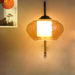 Down Kachori Glass wall light with downward amber glass shade and curved brass arm, glowing warmly on wall