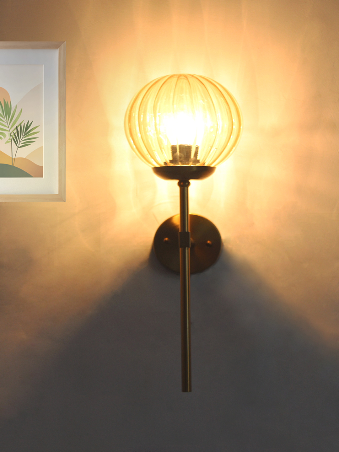 Contemporary Brass Funner Wall Lamp with Amber Kharbuja Glass Amber Kharbuja Glass wall light with ribbed amber glass globe and brass mount, glowing warmly on wall
