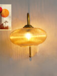Down Ribbed Amber Glass wall light with ribbed amber shade and curved brass arm, casting warm ambient glow on wall