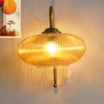 Down Ribbed Amber Glass wall light with ribbed amber shade and curved brass arm, casting warm ambient glow on wall