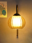 Amber Kharbhuja Glass wall light with ribbed amber glass shade and curved brass arm mounted on wall