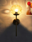 Amber Glass Globe Modern Light wall fixture with textured amber glass globe and brass arm mounted on white wall