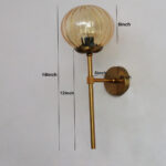 Amber Kharbuja Glass wall light with ribbed amber glass globe and brass mount, glowing warmly on wall