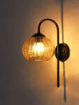 Hanging Black Wall Lamp with amber ribbed glass shade and matte black curved metal wall mount for elegant modern indoor lighting