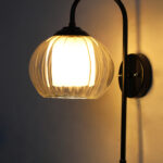 Downward Globe Black Wall Lamp with clear ribbed globe glass shade and matte black curved metal wall mount for elegant modern indoor lighting