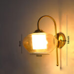 Down Kachori Glass wall light with downward amber glass shade and curved brass arm, glowing warmly on wall