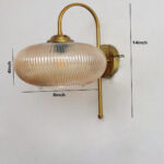 Down Ribbed Amber Glass wall light with ribbed amber shade and curved brass arm, casting warm ambient glow on wall