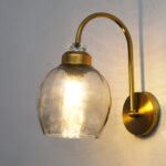 Antique brass smoked glass wall light with curved arm and round wall mount