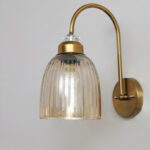 Antique brass wall light with amber ribbed glass shade and curved metal arm, shown with product dimensions.