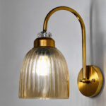 Antique brass wall light with amber ribbed glass shade and curved metal arm, shown with product dimensions.