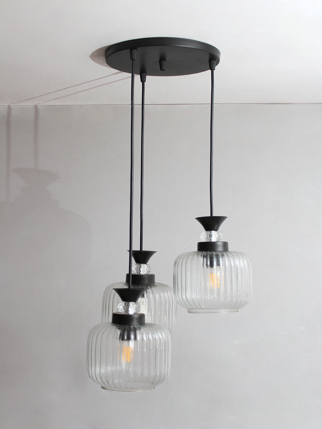 3-Light Clear Ribbed Glass Cluster Hanging Light Clear Ribbed Glass cluster hanging light with three pendant shades, black metal fittings, and adjustable drops for modern dining room and living room interiors.