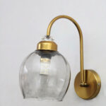 Antique brass smoked glass wall light with curved arm and round wall mount