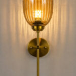 Antique brass wall light with amber ribbed glass shade and curved arm, shown with product dimensions.