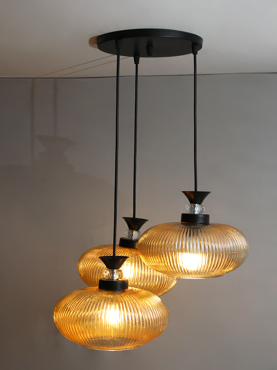 3-Light Amber Ribbed Glass Cluster Hanging Light Amber Ribbed Glass cluster hanging light with four textured glass pendant shades, black metal fittings, and layered design for modern interior lighting.