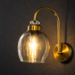 Antique brass smoked glass wall light with curved arm and round wall mount
