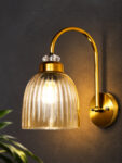 Antique brass wall light with amber ribbed glass shade and curved metal arm, shown with product dimensions.