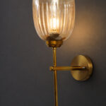 Antique brass wall light with amber ribbed glass shade and curved arm, shown with product dimensions.