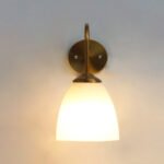 Antique brass wall sconce with curved arm and milky white bell-shaped glass shade.