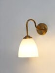 Antique brass wall sconce with curved arm and milky white bell-shaped glass shade.