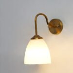 Antique brass wall sconce with curved arm and milky white bell-shaped glass shade.