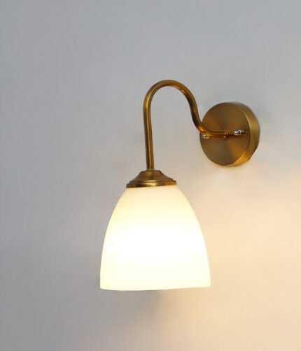 Antique brass wall sconce with curved arm and milky white bell-shaped glass shade.