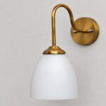 Antique brass wall sconce with curved arm and milky white bell-shaped glass shade.