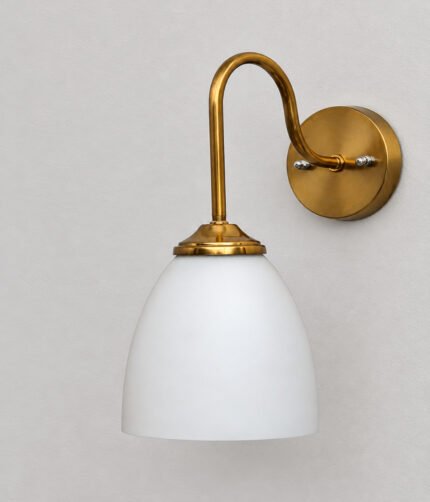 Antique brass wall sconce with curved arm and milky white bell-shaped glass shade.