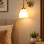 Antique brass wall sconce with curved arm and milky white bell-shaped glass shade.